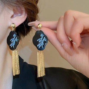 Close-up of long gold tassel earrings with black cloud base and floral bird patterns