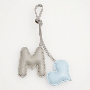 Detailed view of handmade leather M letter bag charm with blue heart and gray pebble texture
