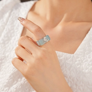 Close-up of a blue resin ring with silver butterfly on a model's finger in white clothing