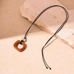 Close-up of a brown resin pendant necklace with silver bead on a textured stone surface