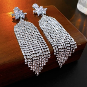 Macro shot of silver tassel earrings with zircon flower studs on a wooden jewelry box