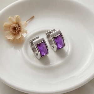 Detail view of silver stainless steel hoop earrings with faceted purple glass crystal