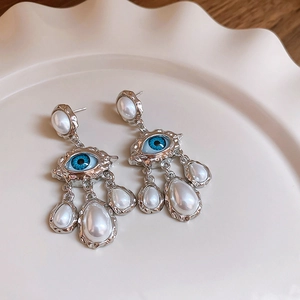Detail of silver vintage evil eye earrings with artificial pearl tassels on ceramic plate