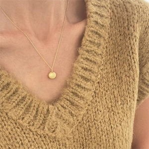 Close-up of a gold shell pendant necklace worn over a cozy beige knit sweater background