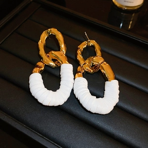 Gros plan de boucles d'oreilles ovales dorées avec cuir blanc sur un plateau noir