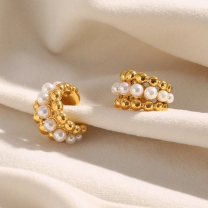 Detail of gold-plated C-shaped ear cuff with white pearls on elegant beige silk