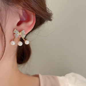 Dettaglio di orecchini a fiocco dorati con strass e perle bianche indossati dalla modella