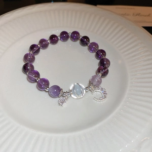 Purple crystal beaded bracelet with moon and star charms on a white ceramic plate