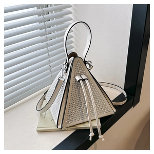 Detail of white pyramid bag with silver studs and drawstring on green books