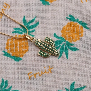 Gold plated cactus necklace featuring green zircon stones on decorative pineapple fabric