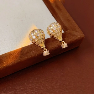 Gros plan sur boucles d'oreilles montgolfière en or et zircons sur velours brun