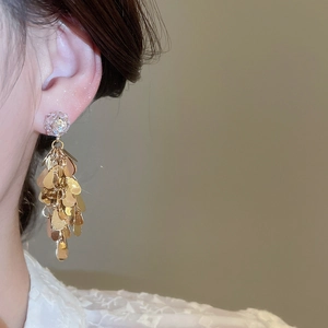 Close-up of gold tassel earrings with clear crystals on model against beige background
