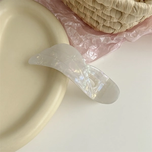 Detailed view of an acetate wing lily hair clip in pearl white on a ceramic dish
