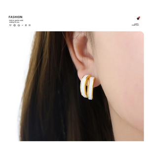 Close-up of dual-layer gold-trimmed white enamel C-shape earrings on female model