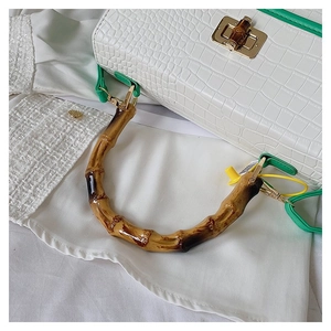 Close-up of white crocodile pattern handbag with bamboo handle and green strap