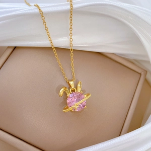 Close-up of pink crystal rabbit pendant on gold chain with soft white silk background