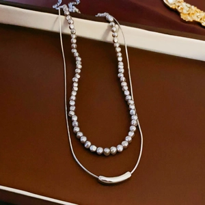 Detail of double-layer silver necklace with delicate beads and curved tube pendant