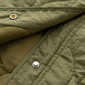 Makroansicht der olivgrünen Steppjacke mit silbernen Druckknöpfen und feiner Steppung