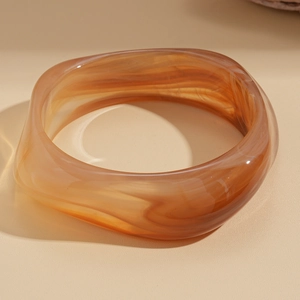 Macro shot of wide acrylic resin bangle with amber marble texture and smooth finish