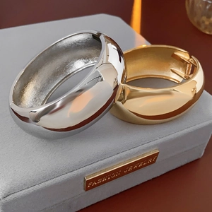 Polished gold and silver wide curved metal bracelets on premium grey velvet jewelry box