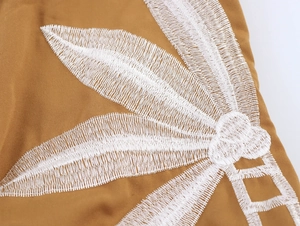 Close-up detail of white leaf embroidery on khaki canvas fabric for the maxi dress