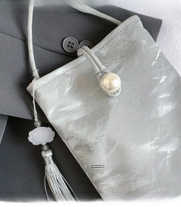 Detailed view of silver-gray textured phone bag with pearl button and lotus tassel