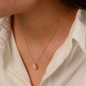 Close-up of gold pear-cut zircon pendant necklace worn with a white shirt