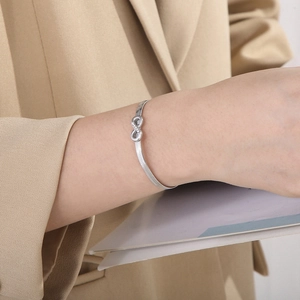 Close-up of silver infinity charm snake chain bracelet worn on wrist with beige blazer