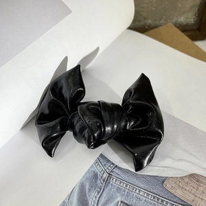 Detail of a shiny black faux leather bow hair clip placed on casual denim fabric background