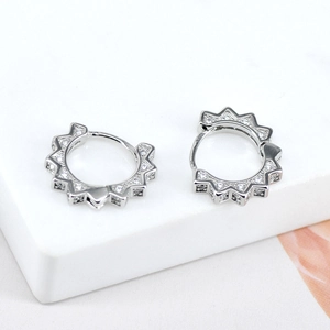 Sparkling silver gear-shaped hoop earrings with zircon pavé setting on marble stand