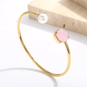 Dettaglio di un bracciale a C dorato con cristallo rosa quadrato e perla tonda lucida