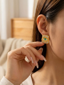 Close-up of gold textured square evil eye earrings with green zircon on model