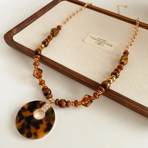 Détail d'un collier doré avec pendentif léopard rond et perles de couleur ambre