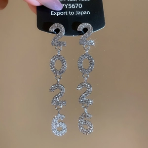 Macro view of silver 2026 number earrings with sparkling rhinestones on black label