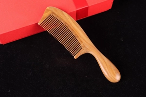 Close-up of a natural sandalwood hair comb with handle and elegant red gift box packaging