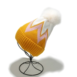 Dettaglio del berretto in maglia con motivo a zigzag giallo rosa e pompon bianco