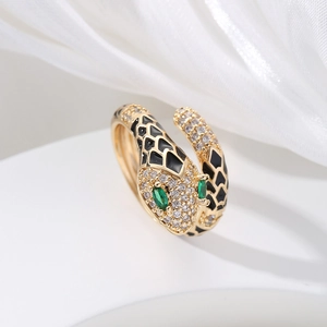 Detail of gold snake ring with black enamel scales and green gemstone eyes