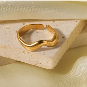 Macro shot of minimalist gold wavy open ring displayed on textured stone and silk