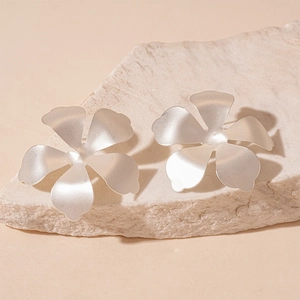 Detailed view of matte silver flower earrings placed on a textured stone pedestal