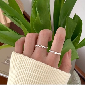 Close-up of minimalist silver twist and wavy open rings worn on fingers in a natural setting