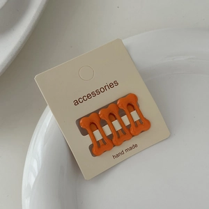Close-up of three orange bone-shaped hair clips on a handmade accessories card