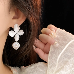 Macro detail of a silver flower earring with a white pearl drop worn by a model