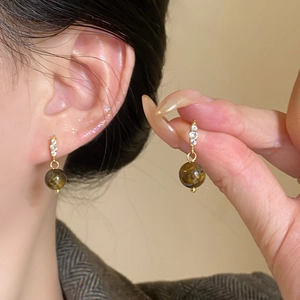 Close-up of gold earrings featuring three round zircons and a brown tiger eye stone