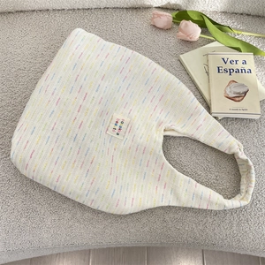 Close-up of a striped knit tote bag with brand label and elegant props layout