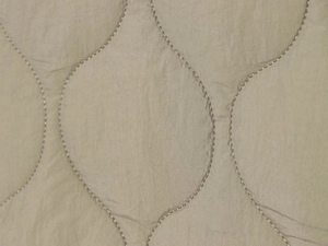 Detailed close-up of wave-quilted fabric texture on a taupe leopard print padded jacket