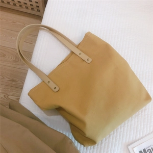 Detail view of ginger yellow canvas tote bag with brown leather handles and metal rivets