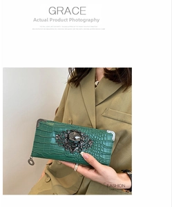 Detail of green crocodile texture clutch with gothic black skull emblem on leather