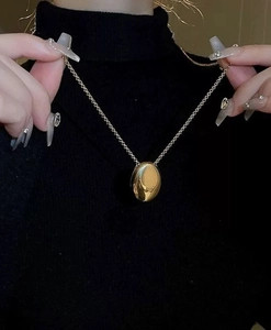 Detailed view of a shiny gold teardrop pendant necklace worn over a black sweater