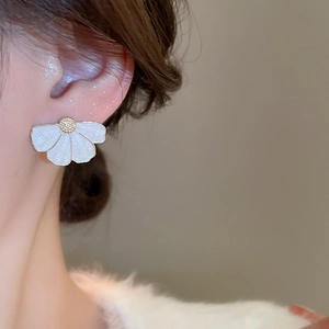 Détail d'une boucle d'oreille fleur en émail blanc avec centre doré portée par un mannequin