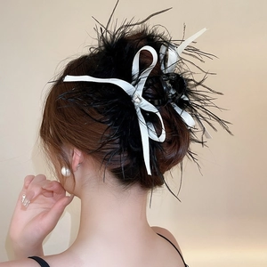 Detail of white satin ribbon and black feather hair claw clip worn on a woman's hair
